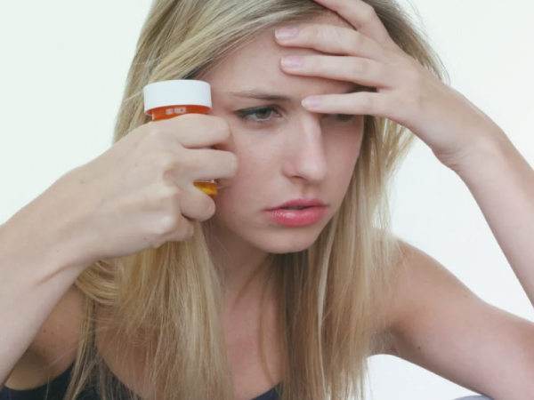 Девушка держа в руке таблетки смотрит вдаль